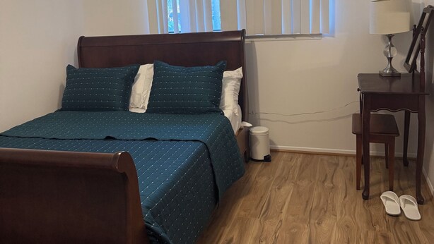 Ein Schlafzimmer mit Bett, Schreibtisch, Stuhl, Deckenventilator und Fenster mit Jalousien.