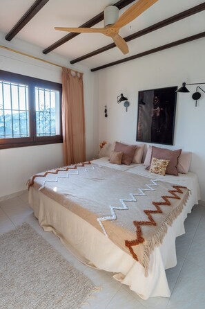 A bedroom with a large bed, a ceiling fan, a window with curtains, and a wall-mounted lamp. - Beautiful villa on the Costa Blanca, with a pool, ocean view, garden, and close to the beach and Dénia. (Pego)
