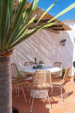 A patio with a round table and wicker chairs, surrounded by terracotta tiles and a white wall. - Beautiful villa on the Costa Blanca, with a pool, ocean view, garden, and close to the beach and Dénia. (Pego)
