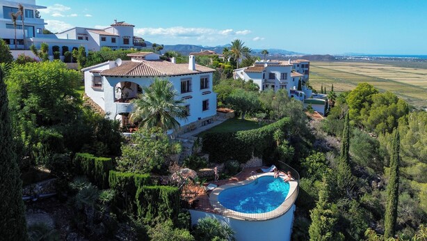 A large house with a swimming pool surrounded by lush greenery and a view of distant fields. - Beautiful villa on the Costa Blanca, with a pool, ocean view, garden, and close to the beach and Dénia. (Pego)