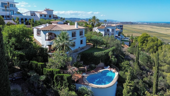 A large house with a swimming pool surrounded by lush greenery and a view of distant fields. - Beautiful villa on the Costa Blanca, with a pool, ocean view, garden, and close to the beach and Dénia. (Pego)