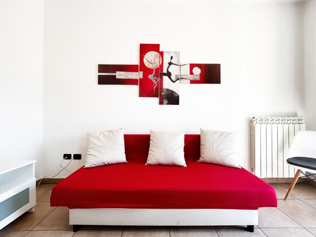 Un dormitorio moderno con una colcha roja, almohadas blancas y una obra de arte abstracta colgada en la pared.