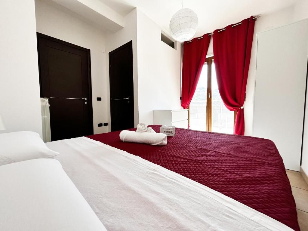 Habitación de hotel con una cama grande, una mesita de noche, una lámpara y una ventana con cortinas rojas.