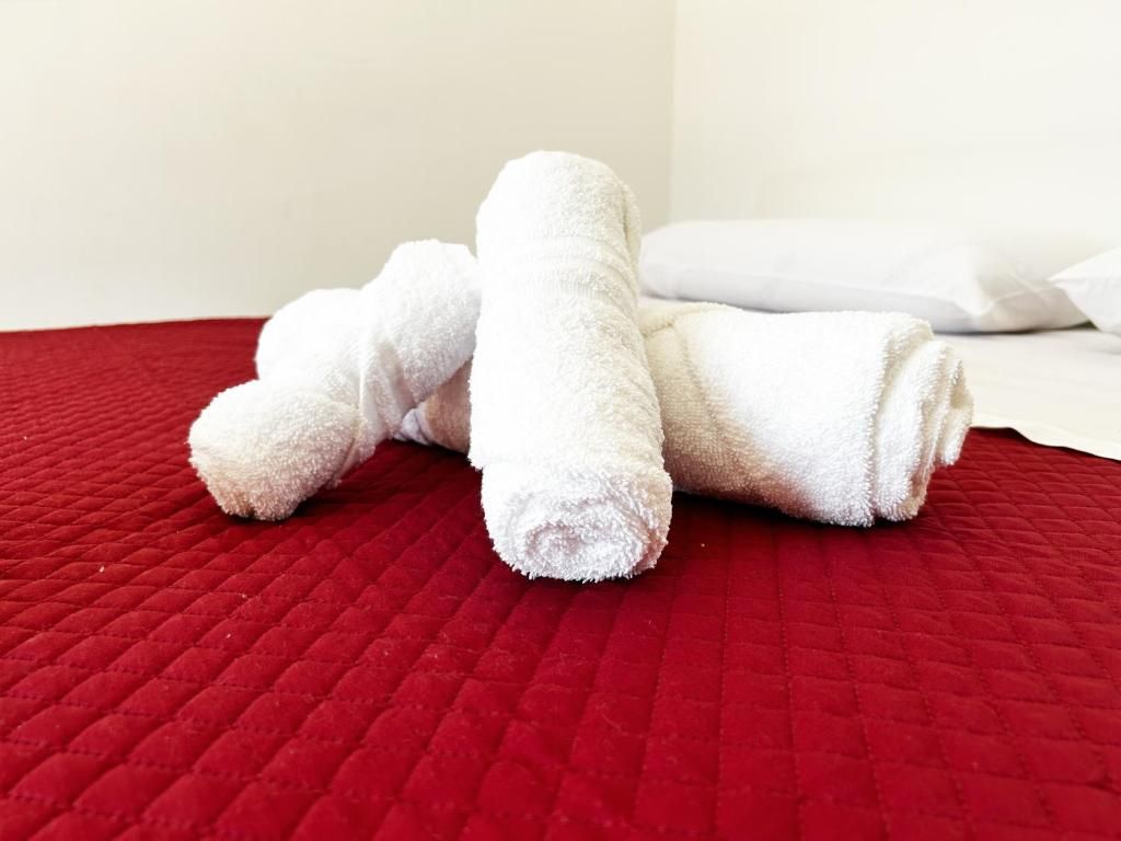 A bed with a red quilted cover and two rolled white towels.