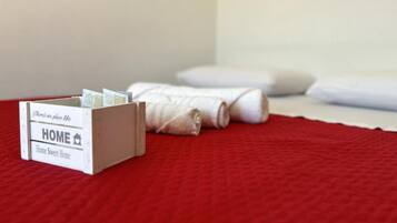 Ein Bett mit weißen Laken und einer rot gesteppten Tagesdecke.