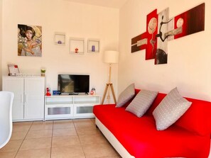 A living room with a red sofa, a television, and artwork on the walls.