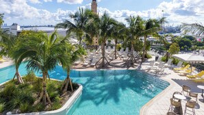 A pool area with lounge chairs and palm trees, a clear sky, and a distant view of a city skyline. - Spacious Corner Stay with Balcony and Pool in Miami G3302 (Miami)