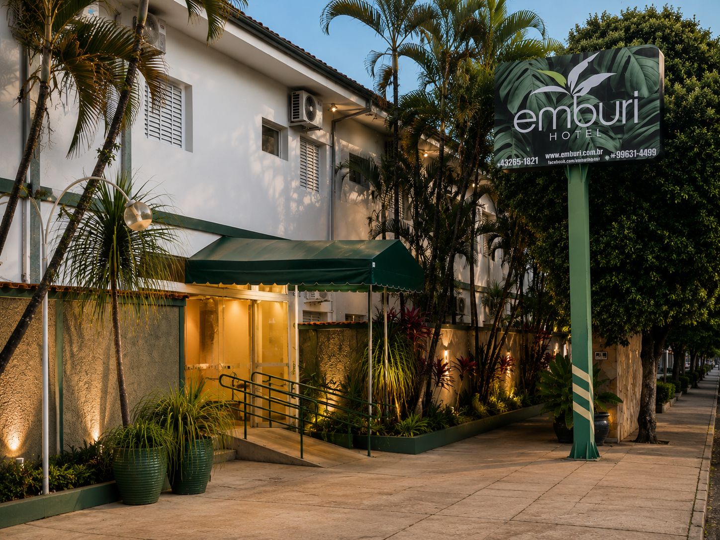 Entrada de hotel con un corredor cubierto, palmeras y un cartel.