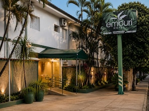 A hotel entrance with a covered walkway, palm trees, and a signboard.
