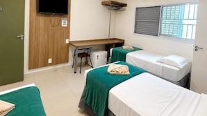 Habitación de hotel con dos camas, un escritorio, una silla, un televisor y una ventana con persianas.