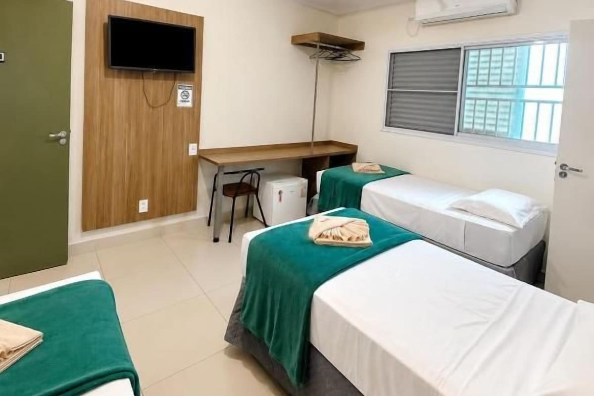 A hotel room with two beds, a desk, a chair, a television, and a window with blinds.