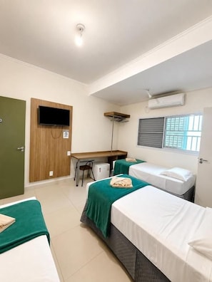 A hotel room with two beds, a desk, a chair, a television, and a window with blinds. - Hotel Emburi (Piratininga)