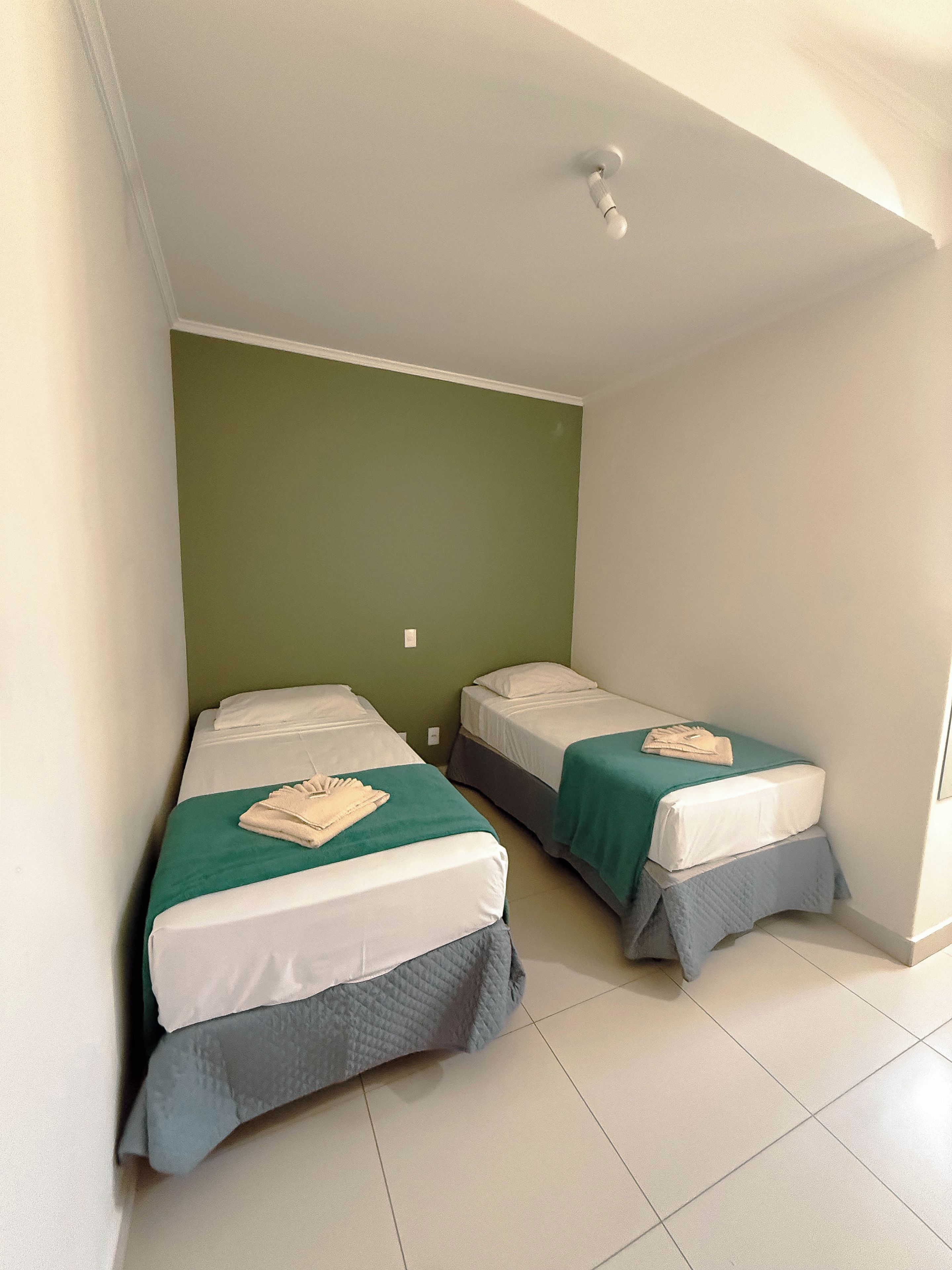 A room with two single beds, each with a green bedspread and white linens.