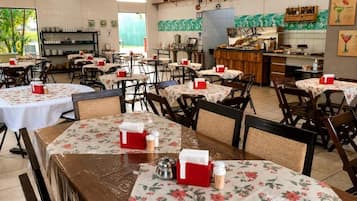 Un restaurante con varias mesas, sillas y una zona de cocina.