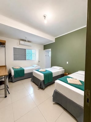 A room with three beds, a desk, and a window with blinds. - Hotel Emburi (Piratininga)