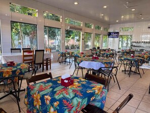 An indoor dining area with tables covered in tropical prints, large windows, and ceiling fans. - Hotel Emburi (Piratininga)