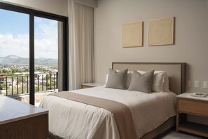 Ein Hotelzimmer mit einem großen Bett, einem Schreibtisch und Blick auf eine Stadtlandschaft vom Balkon aus.