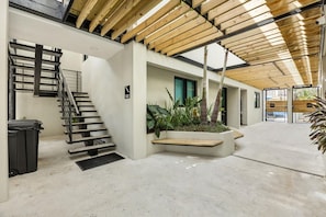 Ein modernes Interieur mit Betonboden, einer Holztreppe, einem Pflanzenbeet und Meerblick durch eine Glastür.