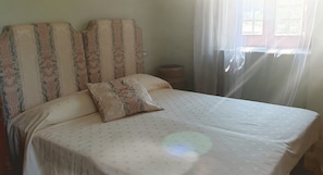 A bed with a patterned headboard and a single pillow, a bedside table, and a window with curtains. - Tramonti d'Agrumi Annex (Naso)