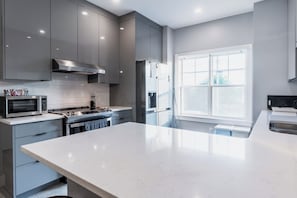 A modern kitchen with grey cabinetry, a stainless steel range, a microwave, and a large window providing natural light.