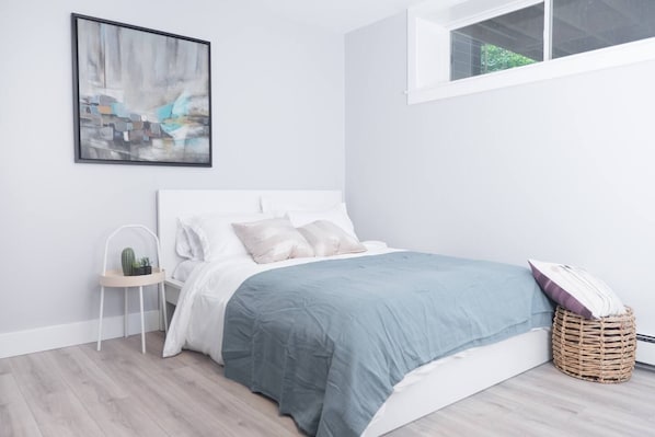 A bedroom with a bed, a nightstand, a cactus, a window, and a wall-mounted painting.