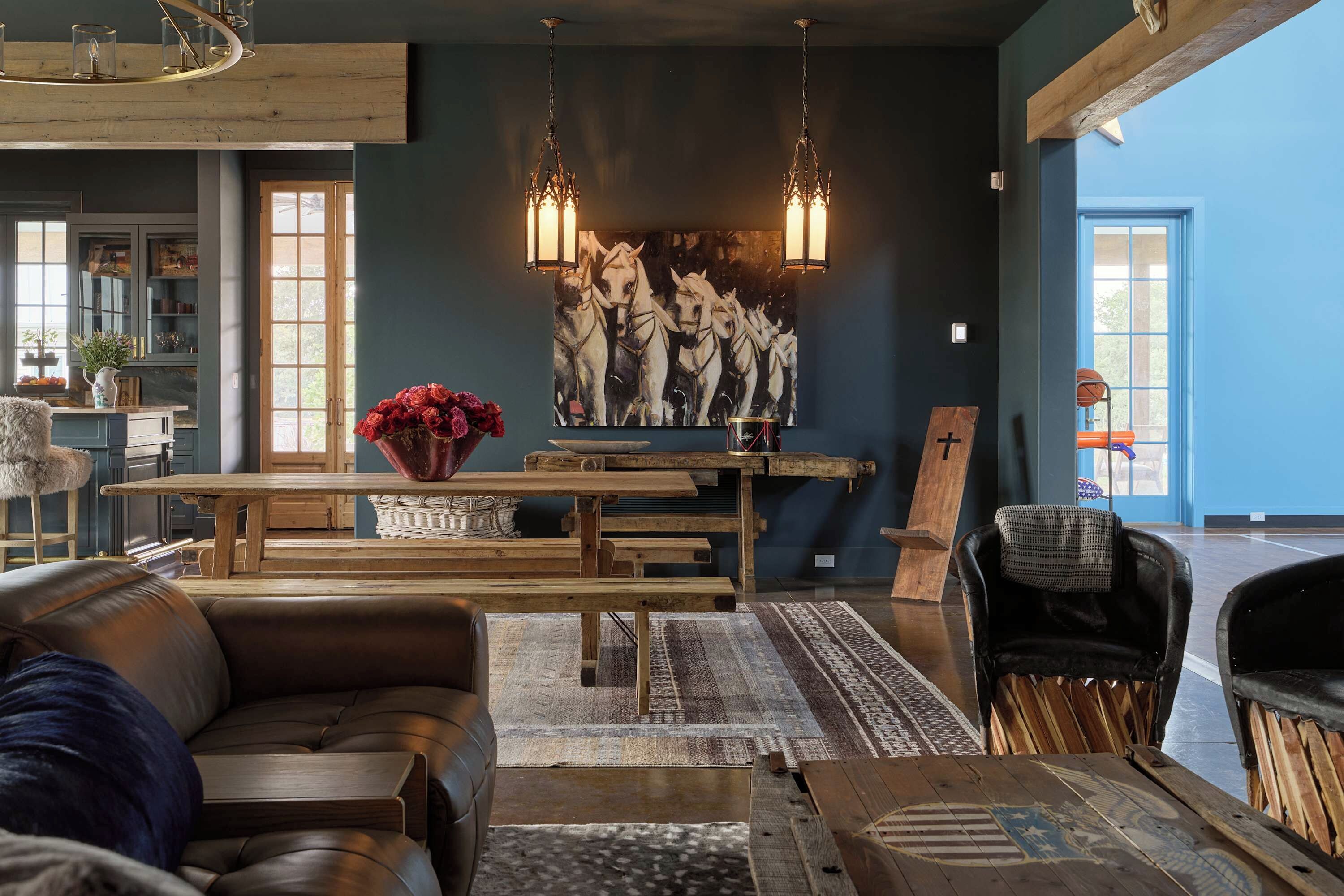 A spacious living room with a large wooden table, leather sofas, and a wall-mounted painting of horses.