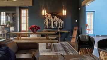A spacious living room with a large wooden table, leather sofas, and a wall-mounted painting of horses.