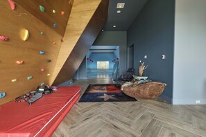 A modern room with a climbing wall, a red sofa, and a herringbone floor pattern. - Hope Ranch | Lux Estate w/ Resort Style Amenities (Round Top)