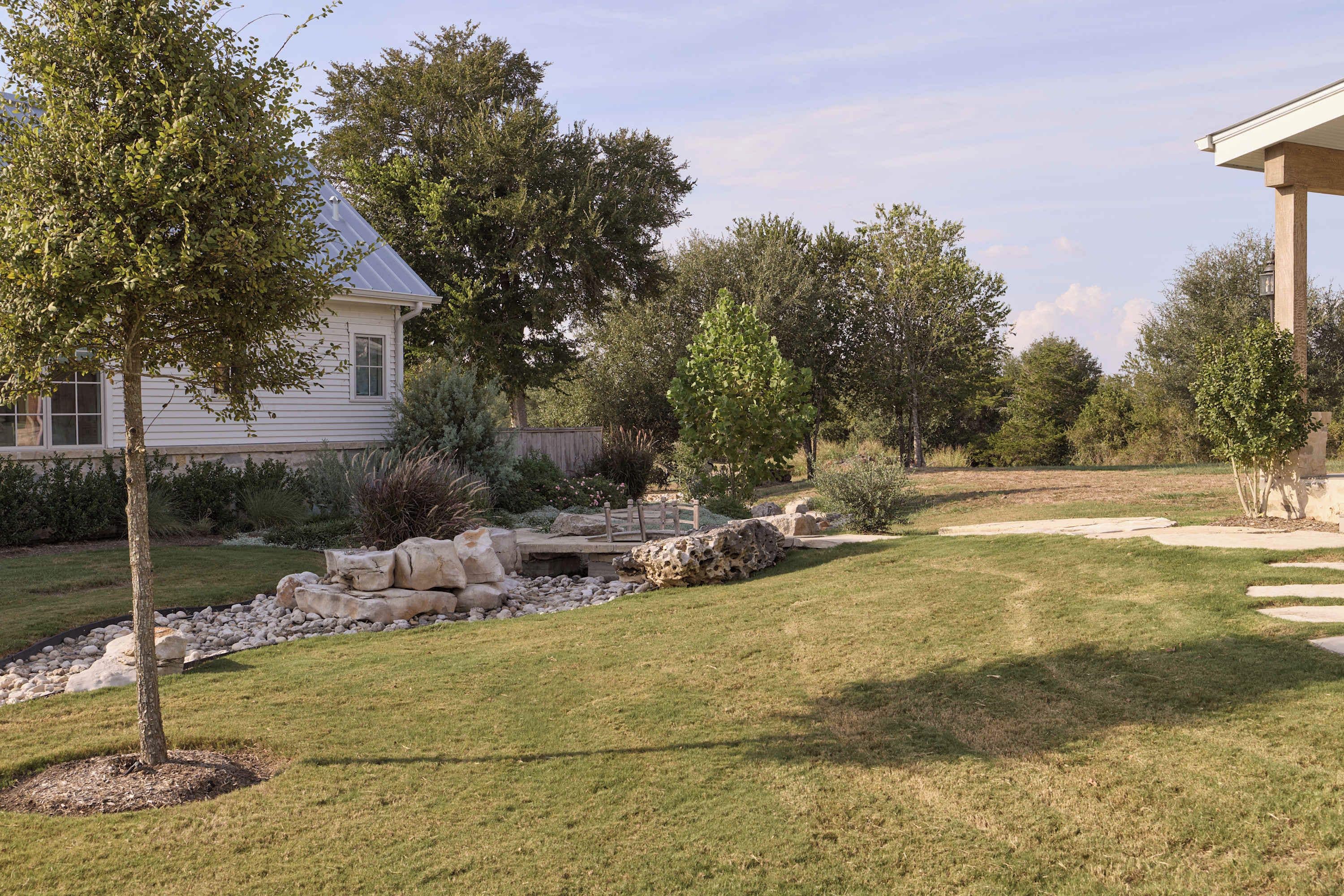 A residential property with a well-maintained lawn, a stone pathway, and a variety of trees.