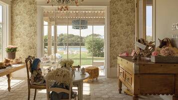 A room with a large window, a chandelier, a wooden table, and a cabinet with decorative items.