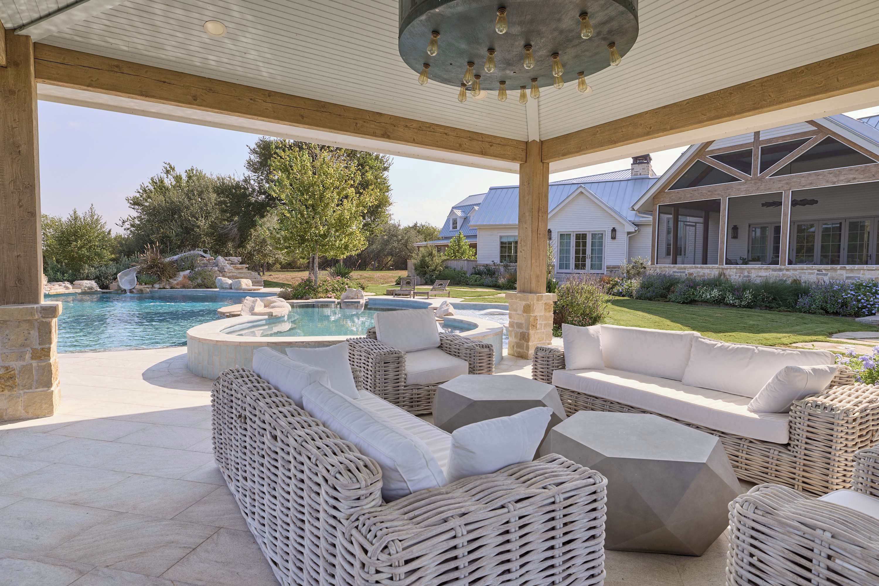 A covered outdoor seating area with wicker furniture and a pool.