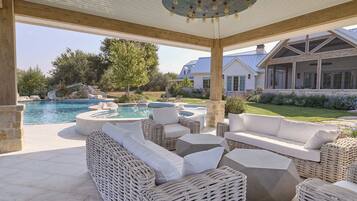 A covered outdoor seating area with wicker furniture and a pool.