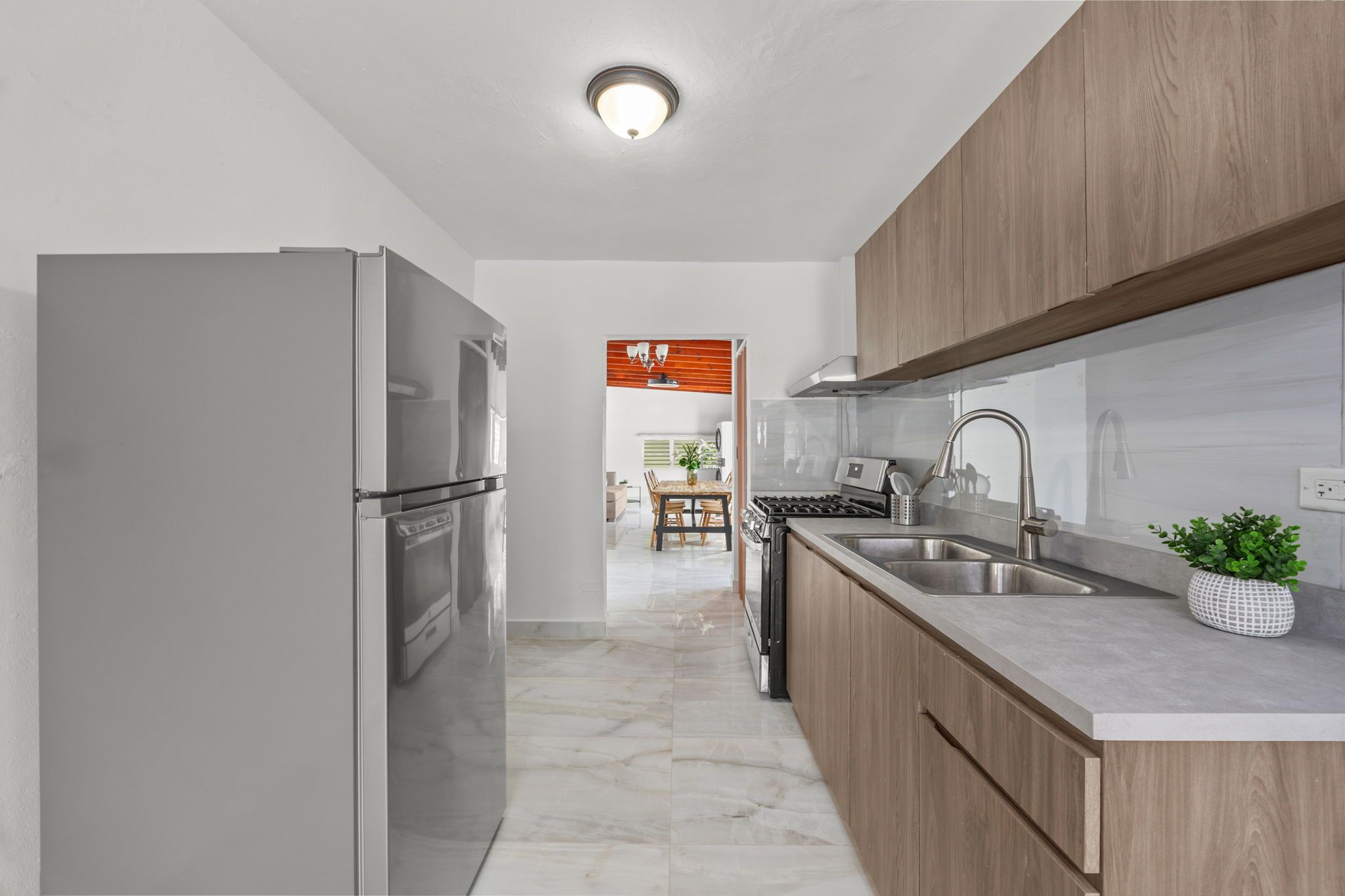 Cozinha moderna com eletrodomésticos de aço inoxidável, armários de madeira e piso de mármore.