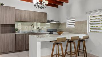 Et moderne køkken med en central ø, barstole og en hængende lampe.