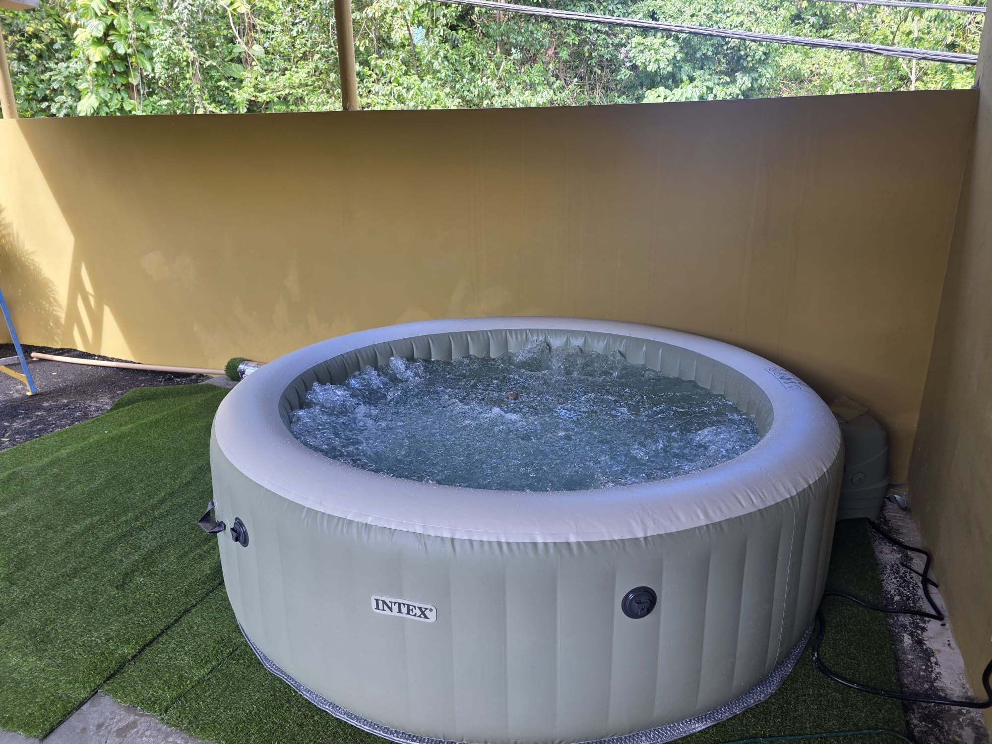 Ein runder Whirlpool mit sichtbarem Firmenlogo, umgeben von Kunstgrastritt und einer gelben Wand.