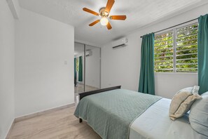 Un dormitori amb un llit, un ventilador de sostre, una finestra amb cortines i un mirall.