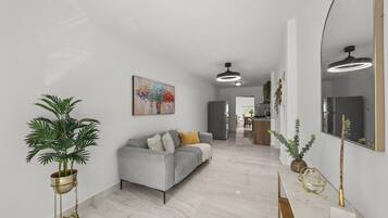 Et moderne interiør med en grå sofa, et stort spejl og et spiseområde i baggrunden.