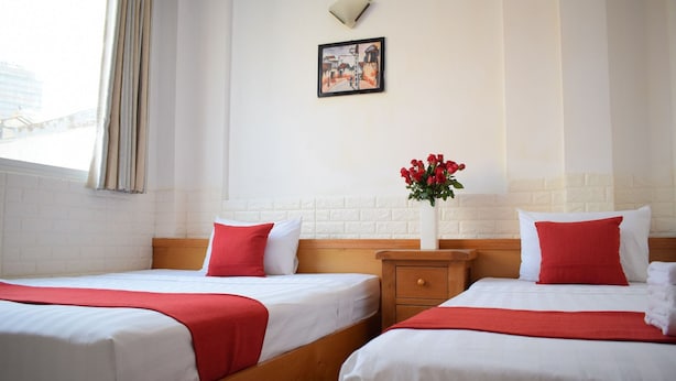 Habitación de hotel con dos camas, una mesita de noche, un jarrón con flores y un cuadro en la pared.