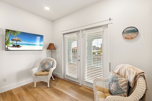 Ein Zimmer mit Fernseher im Strandstil, Korbstühle, einer runden Uhr und einer Schiebetür.