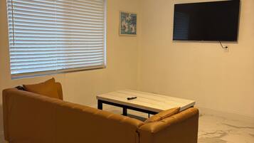 A living room with a sofa, a coffee table, a ceiling fan, a TV, and a window with blinds.
