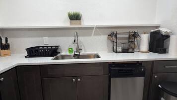 A kitchen with a stainless steel dishwasher, a sink with a faucet, a countertop with a knife block, and a small potted plant on the wall.