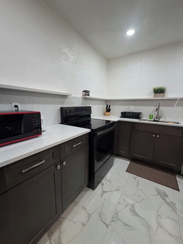 A kitchen with a microwave, stove, sink, and cabinets.