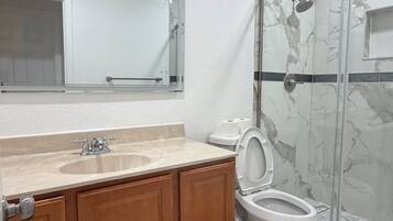 A bathroom with a marble sink, wooden cabinets, a toilet, and a glass shower enclosure.