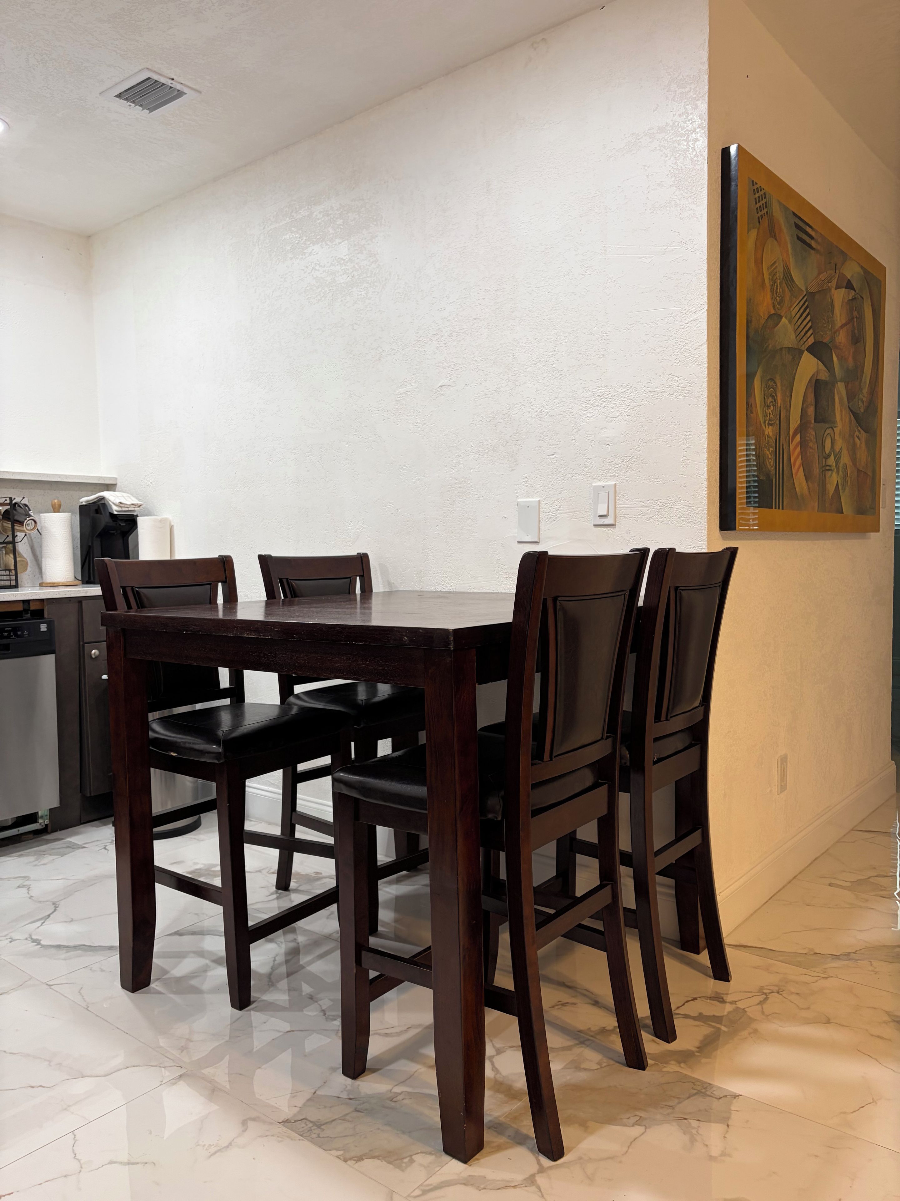 A dining area with a marble floor, a dark wooden table, and four chairs.