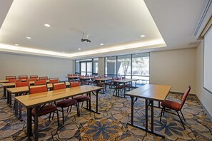 Une salle de conférence équipée de tables et de chaises, de grandes fenêtres et d’un projecteur fixé au plafond.