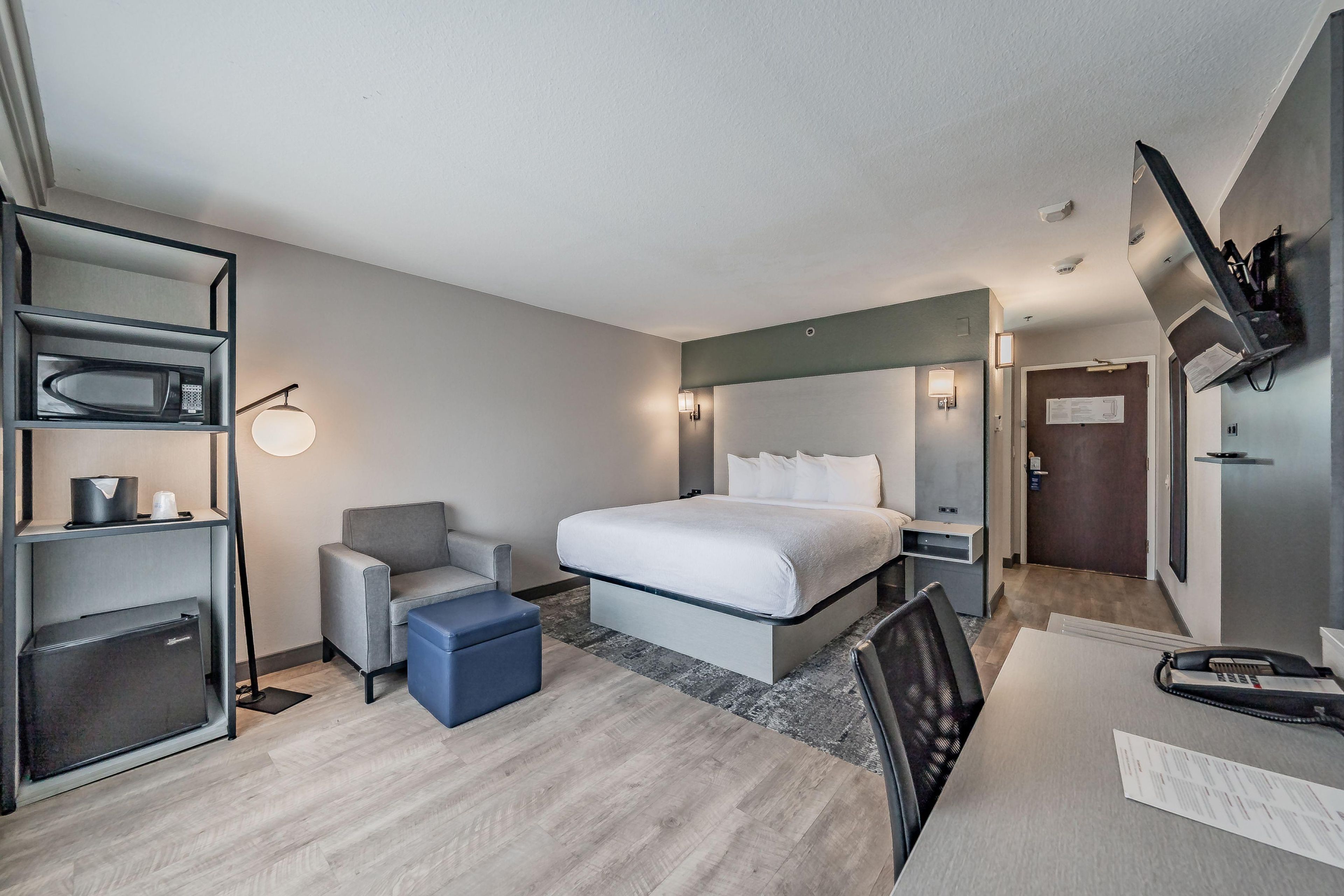 A hotel room with a bed, a desk, a chair, a microwave, and a TV mounted on the wall.