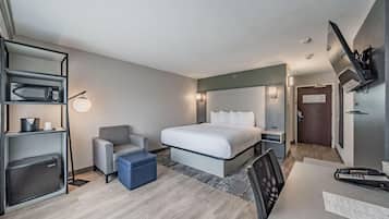 A hotel room with a bed, a desk, a chair, a microwave, and a TV mounted on the wall.
