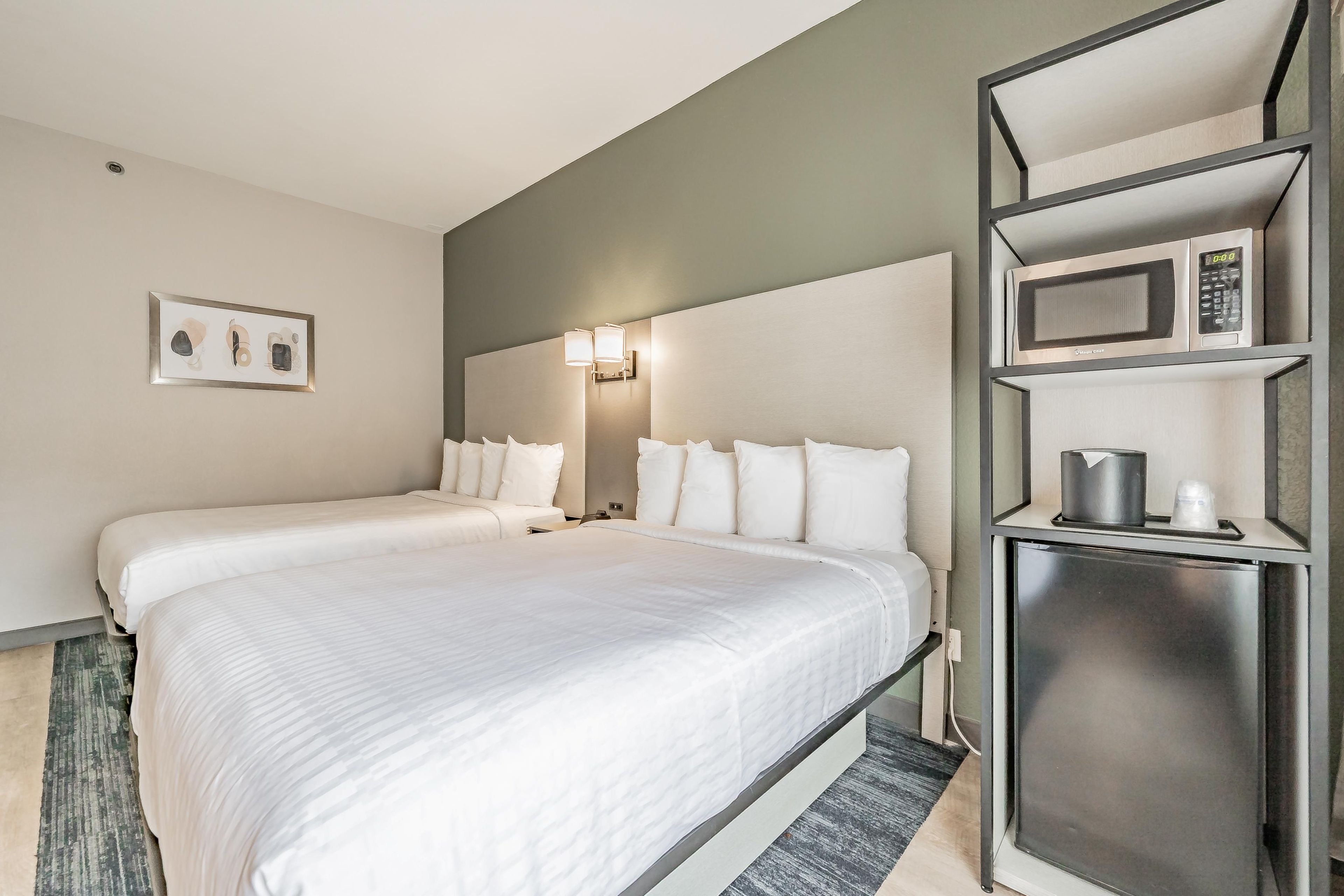 A hotel room with two beds, a microwave, a coffee maker, and a framed picture on the wall.