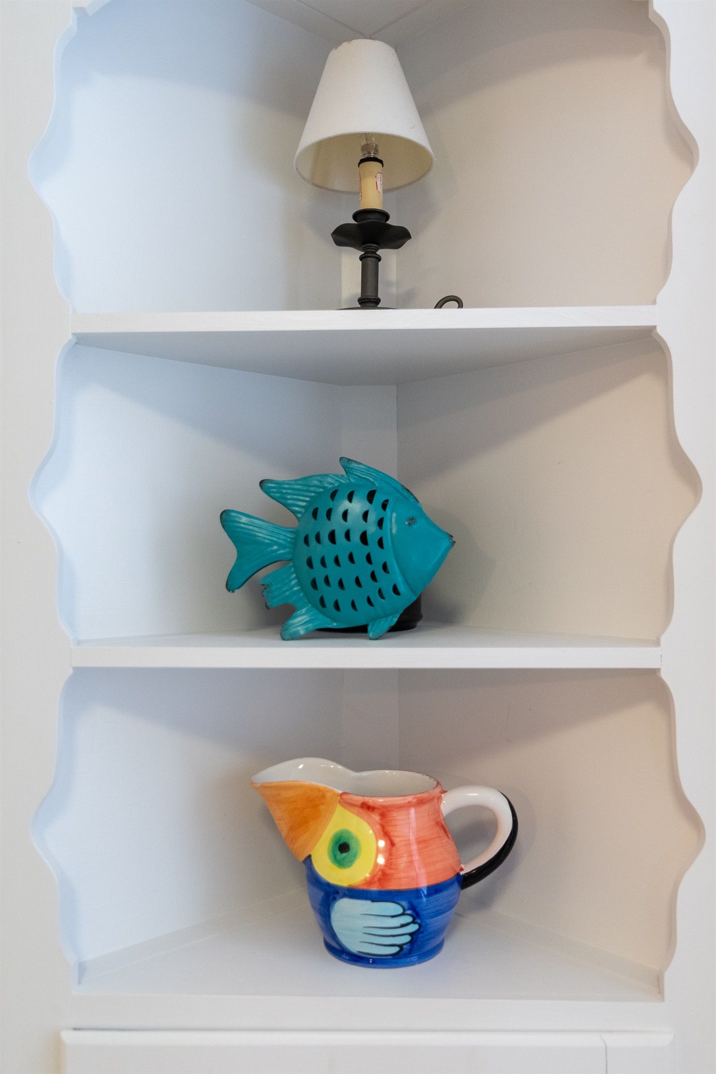Une étagère blanche avec une lampe, un objet bleu en forme de poisson et une tasse colorée également en forme de poisson.