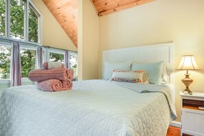 A bedroom with a large bed, a nightstand with a lamp, and a window with curtains.